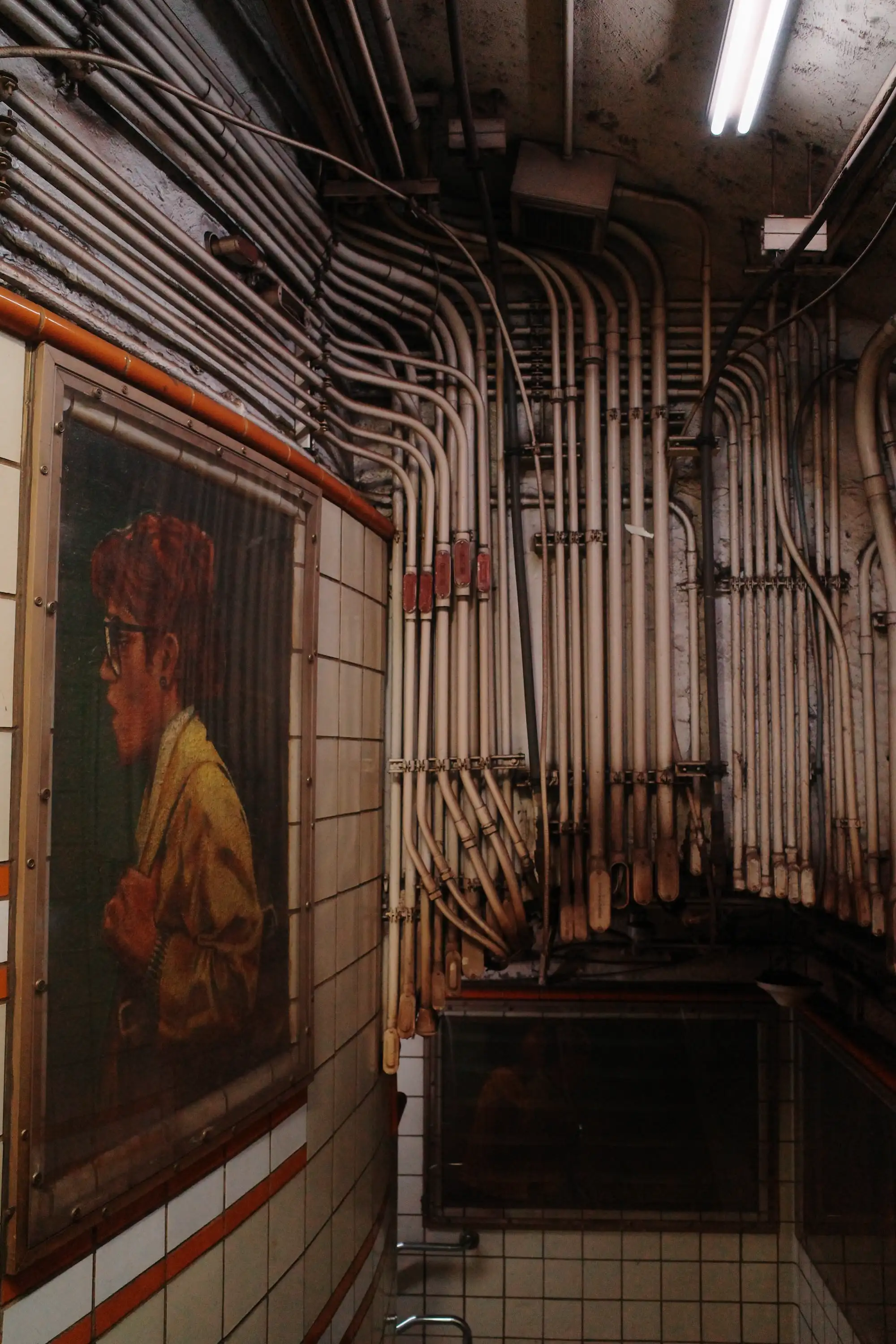 A painted portrait beside a wall of exposed pipes